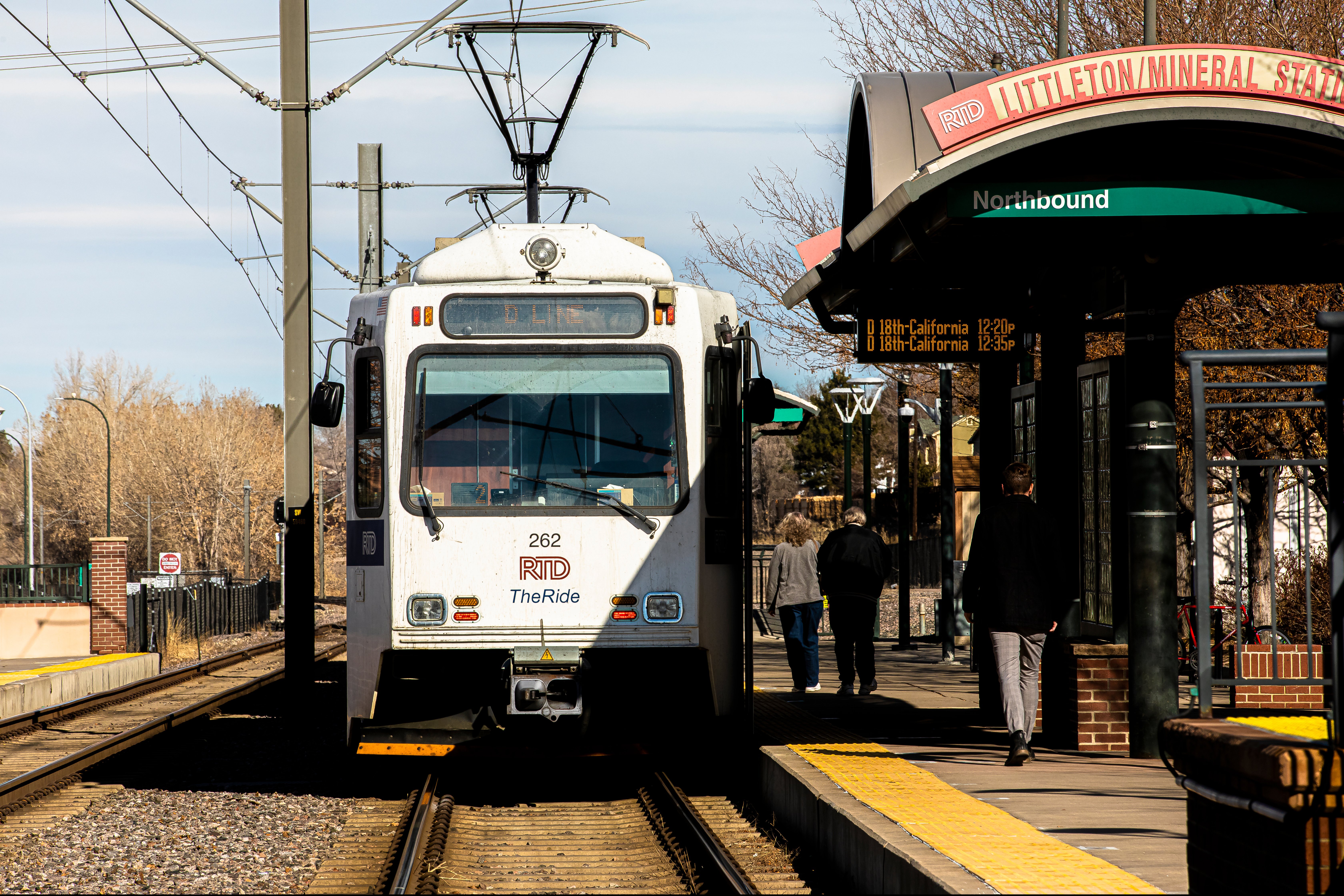 A light rail train arriving at a station with passengers waiting on the platform.