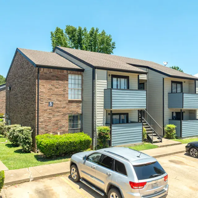 Exterior view of a two-story apartment complex with brick and gray siding, featuring several balconies and well-maintained landscaping.