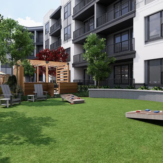 A landscaped courtyard of an apartment complex featuring green grass, lounging chairs, and wooden game tables.