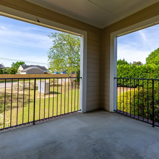 View from a balcony showing a yard with green bushes and trees, and houses in the background.