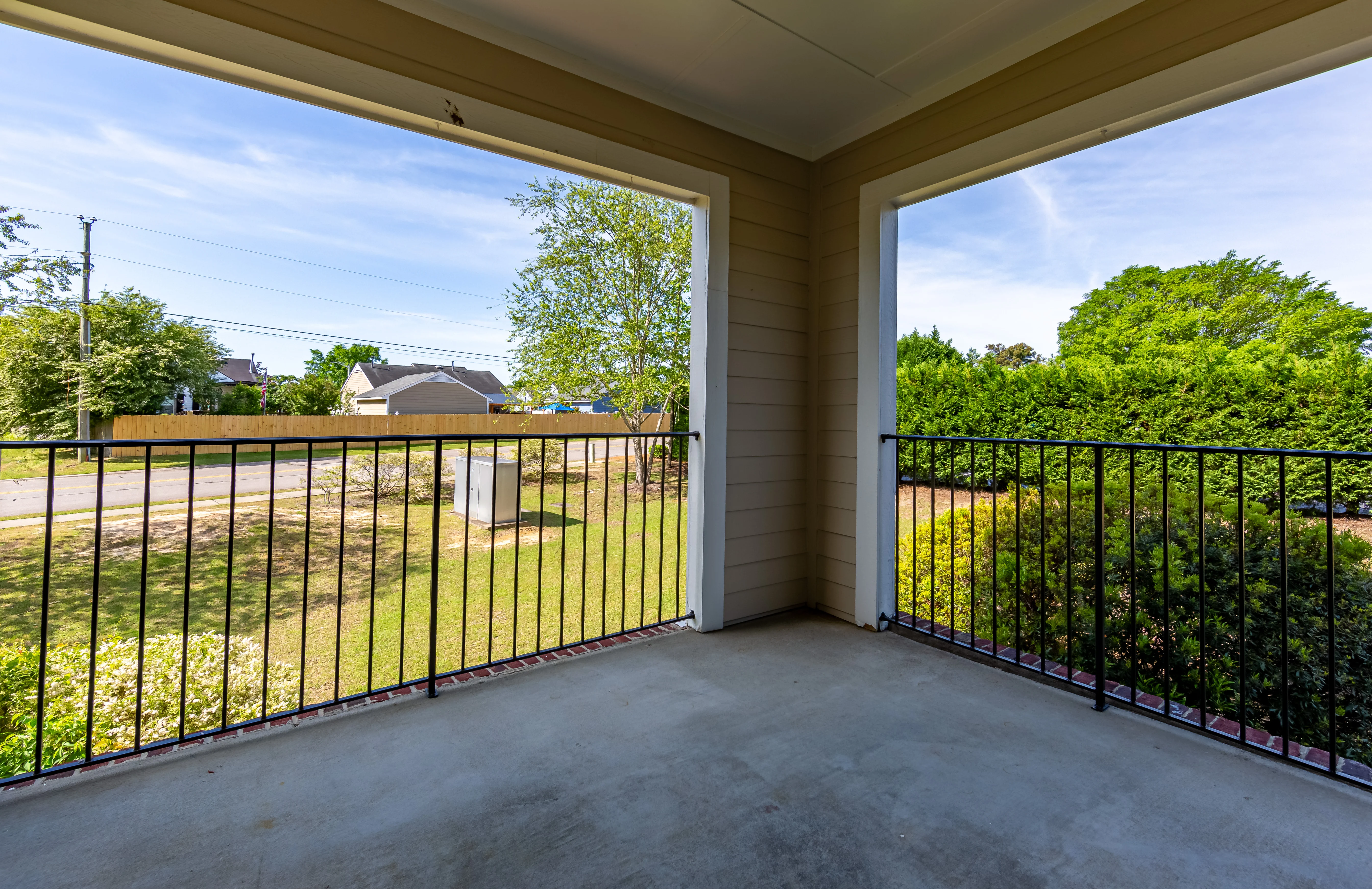 View from a balcony showing a yard with green bushes and trees, and houses in the background.