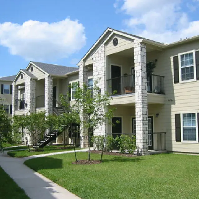 Exterior view of a multi-unit apartment building with stone accents, two levels, and landscaped grassy area.