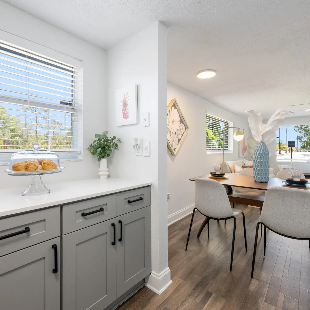 A bright, modern dining area featuring a table with light-colored chairs, a stylish centerpiece, and large windows that let in natural light.