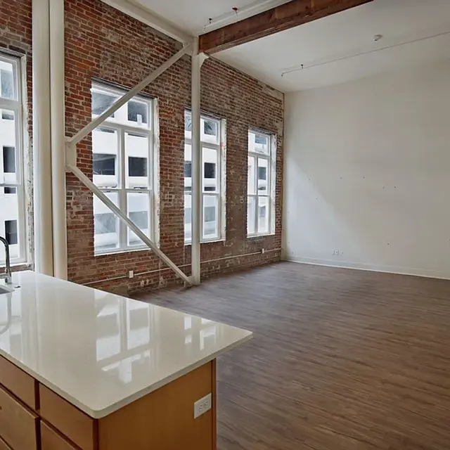 Spacious industrial-style apartment with exposed brick walls and large windows, featuring a modern kitchen island.