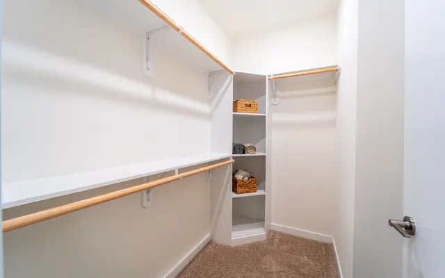 Organized Closet Space A spacious, organized closet interior featuring white shelves, wooden hanging rods, and decorative baskets on a built-in shelf.