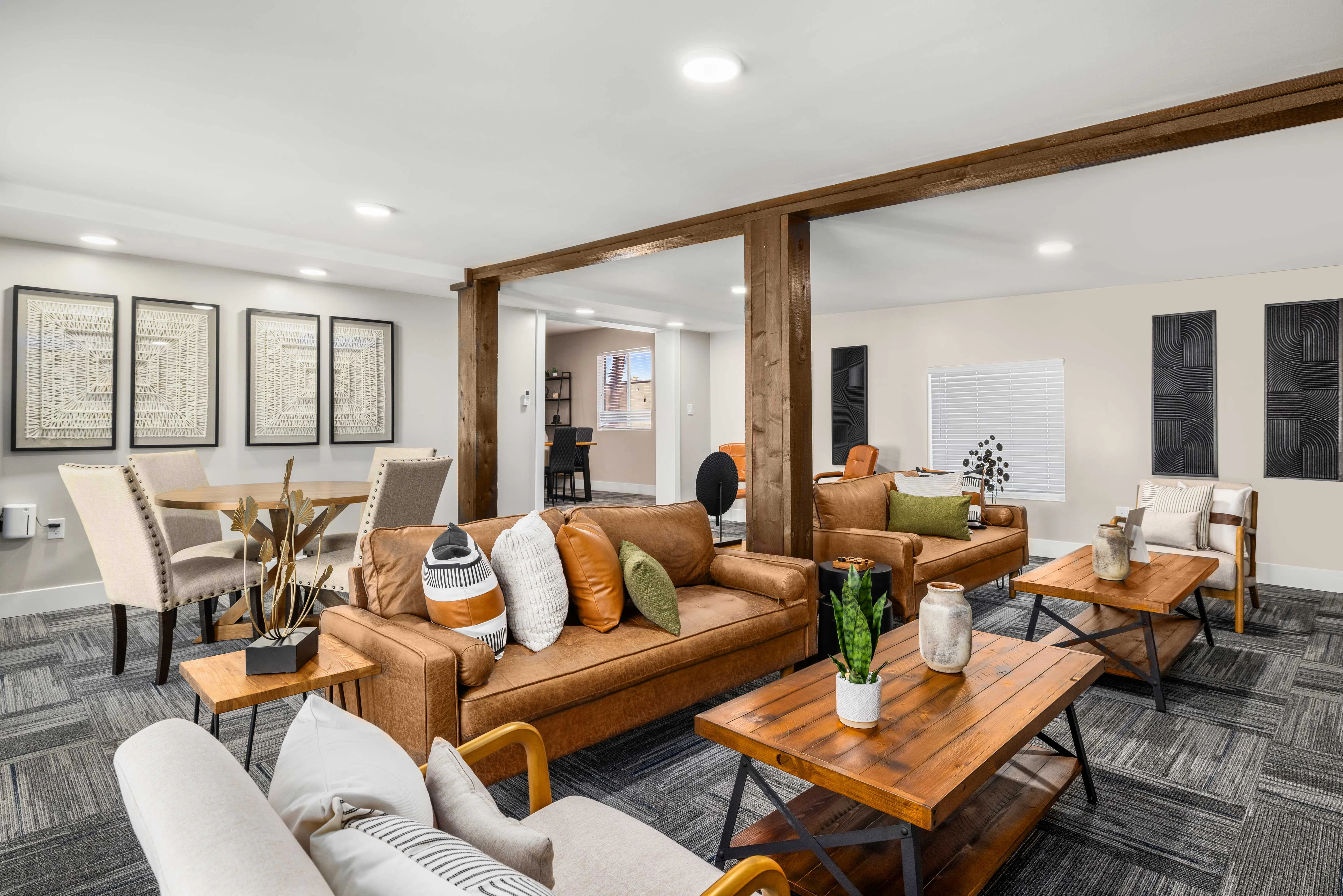 A stylish modern living room featuring brown leather and beige sofas, wooden coffee tables, and decorative plants. The walls are adorned with framed art, adding a contemporary touch to the design.