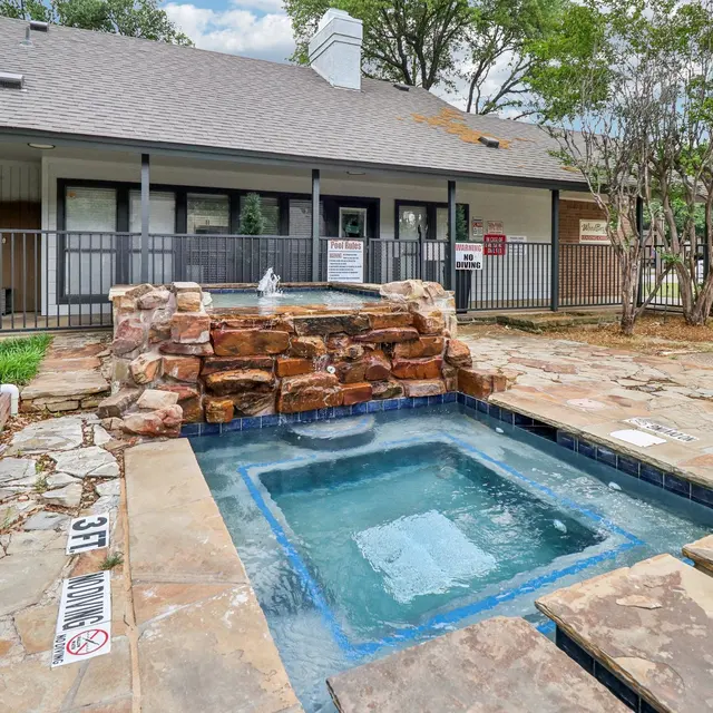 A view of a stone patio with a small jacuzzi and a pool area in an apartment complex.