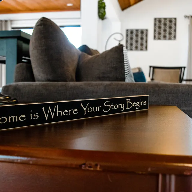 A cozy living room setting with a decorative sign on a wooden table that reads 'Home is Where Your Story Begins.'