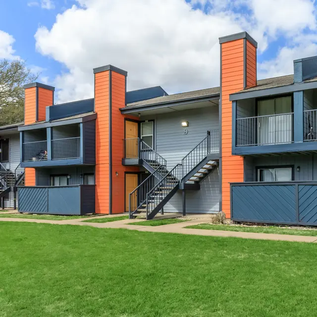 A modern two-story apartment complex featuring vibrant orange and blue walls, with balconies on the upper levels and staircases leading to the entrances.