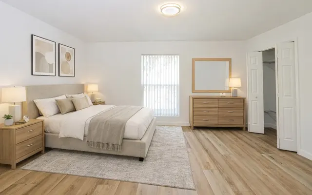 Modern Bedroom Interior A modern bedroom featuring a bed with neutral-colored bedding, two lamps on bedside tables, a large dresser, and art on the walls. The room has hardwood flooring and natural light coming in from a window.