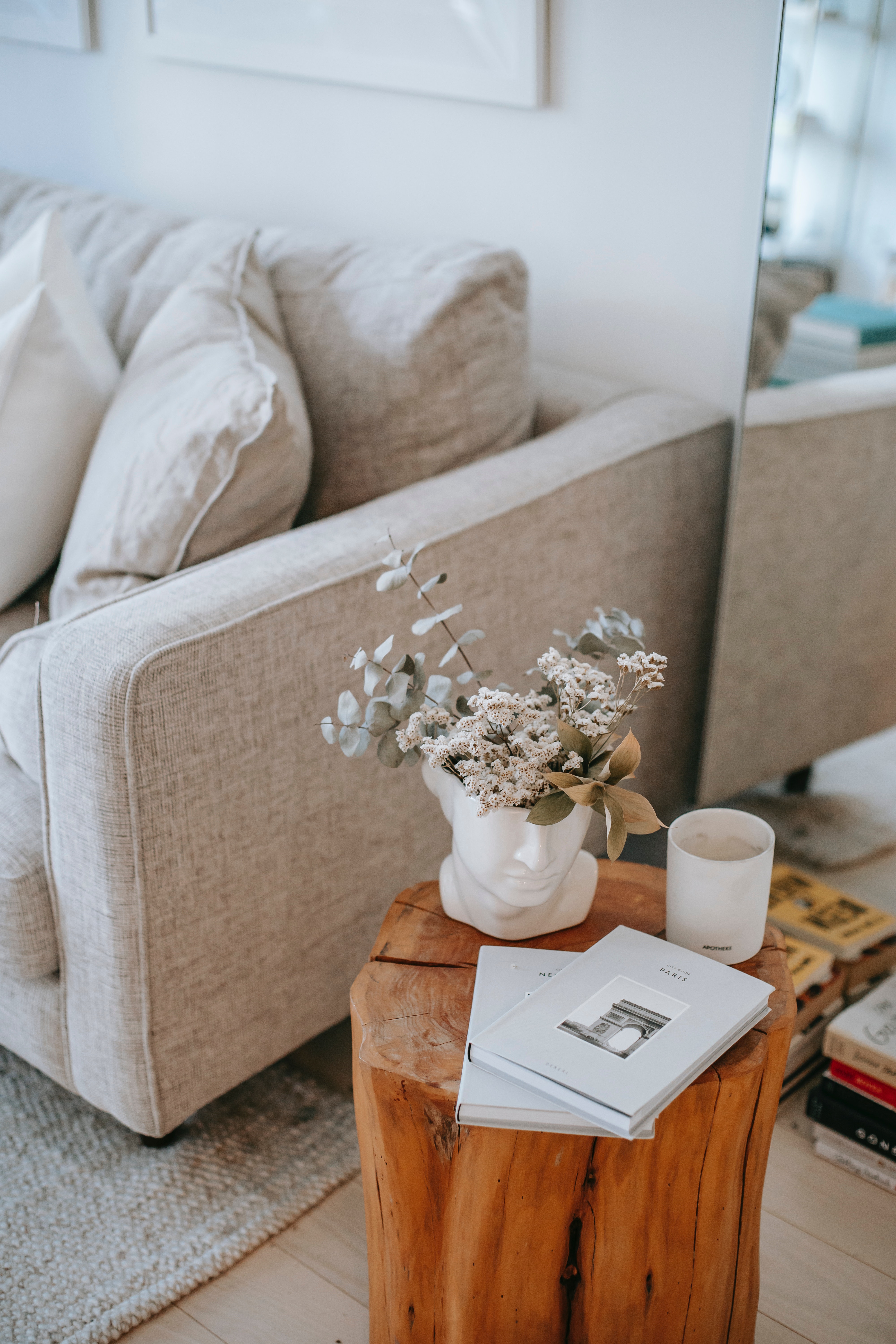 Cozy Living Room Decor A cozy living room featuring a light gray couch, a wooden side table with a decorative vase of flowers, a candle, and a stack of magazines.