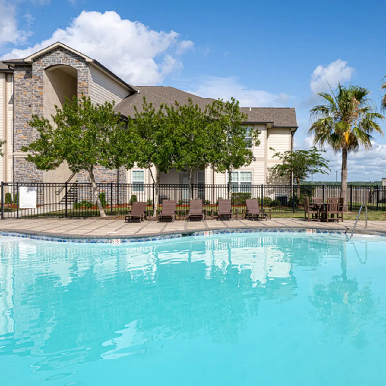 Swimming pool area at an apartment complex with sun loungers and palm trees