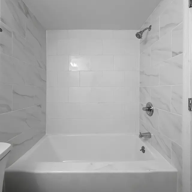 Modern Bathroom Interior A clean and modern bathroom featuring a white tiled shower area and a bathtub. The walls are adorned with light-colored tiles, enhancing the spacious feel of the room. A sleek faucet and shower control are visible, along with a white toilet on the left.