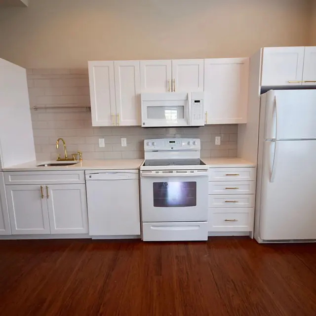 Modern Kitchen Design A bright and modern kitchen featuring white cabinetry, a stainless steel microwave, an oven, and a refrigerator. The kitchen has a light atmosphere with wooden flooring and a simple backsplash.