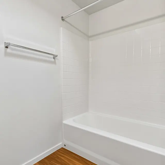 Empty Bathroom Interior A clean and empty bathroom featuring a white bathtub, white tiled walls, and a wooden floor. The space includes a towel bar and a shower fixture.