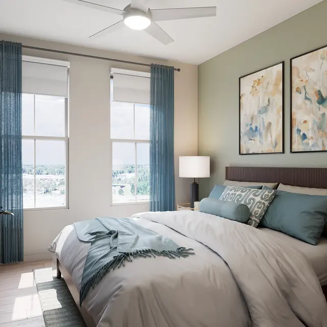 A modern bedroom featuring a queen-sized bed with light gray bedding and decorative pillows, a bedside table with a lamp, two windows dressed with blue curtains, and two floral artworks on the walls, creating a serene atmosphere.