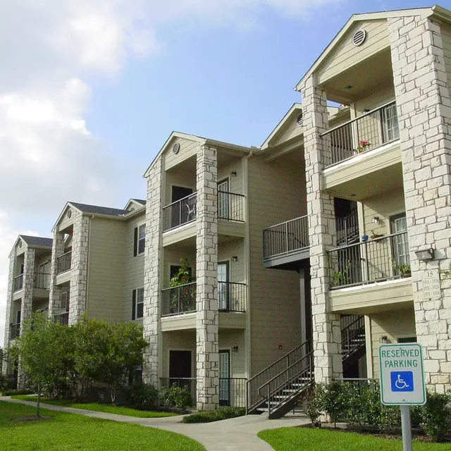 A view of a multi-story apartment building featuring stone and wood siding, with balconies and a winding walkway in a landscaped area.