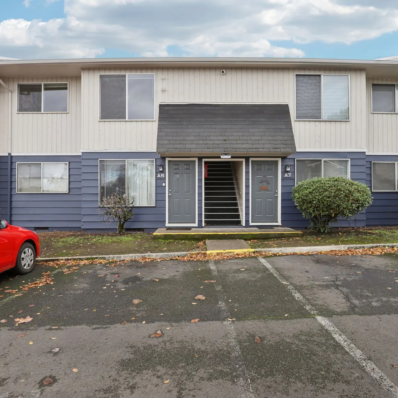 Front view of a two-story apartment complex with blue and white siding and a red car parked nearby.