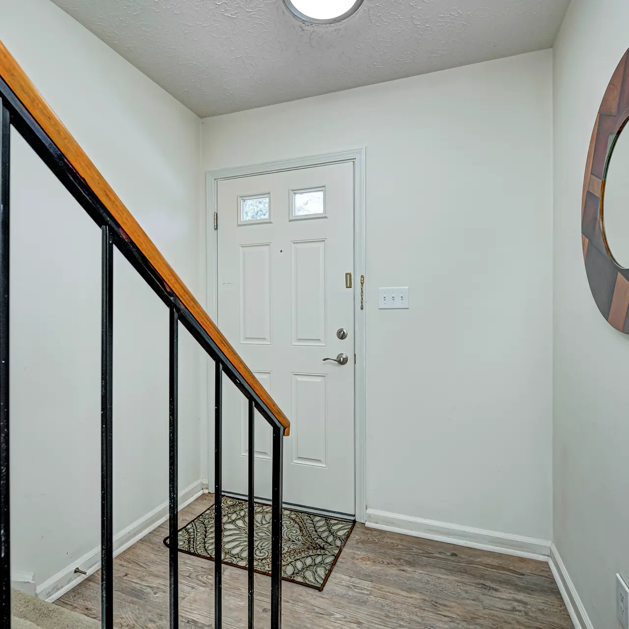 Modern Staircase Entryway Interior of an entryway showing a staircase with a wooden railing, a front door, and a round wall mirror.