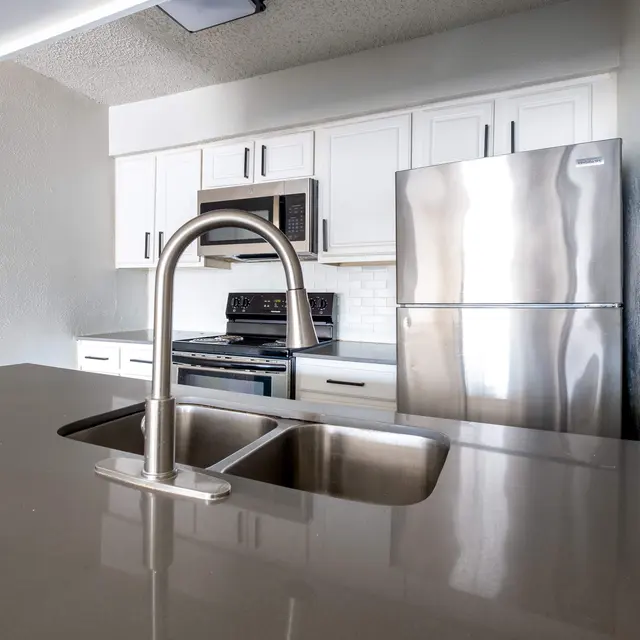 A modern kitchen featuring stainless steel appliances, a double sink, and sleek white cabinetry.