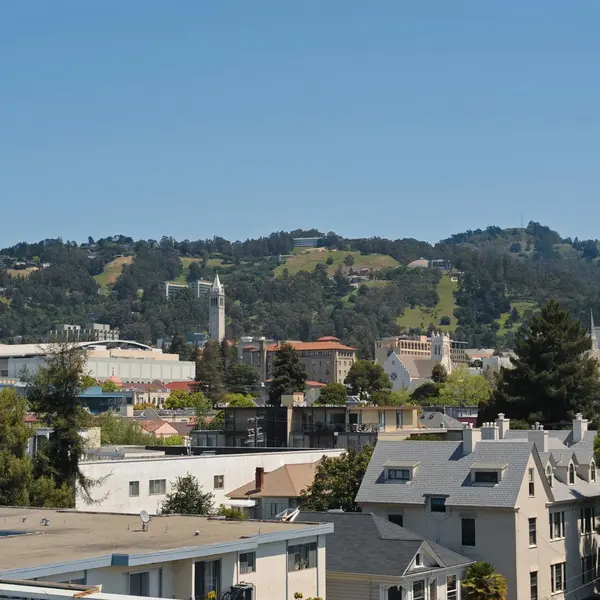 A panoramic view of a cityscape featuring a mix of modern and historic buildings, with green hills in the background under a clear blue sky.