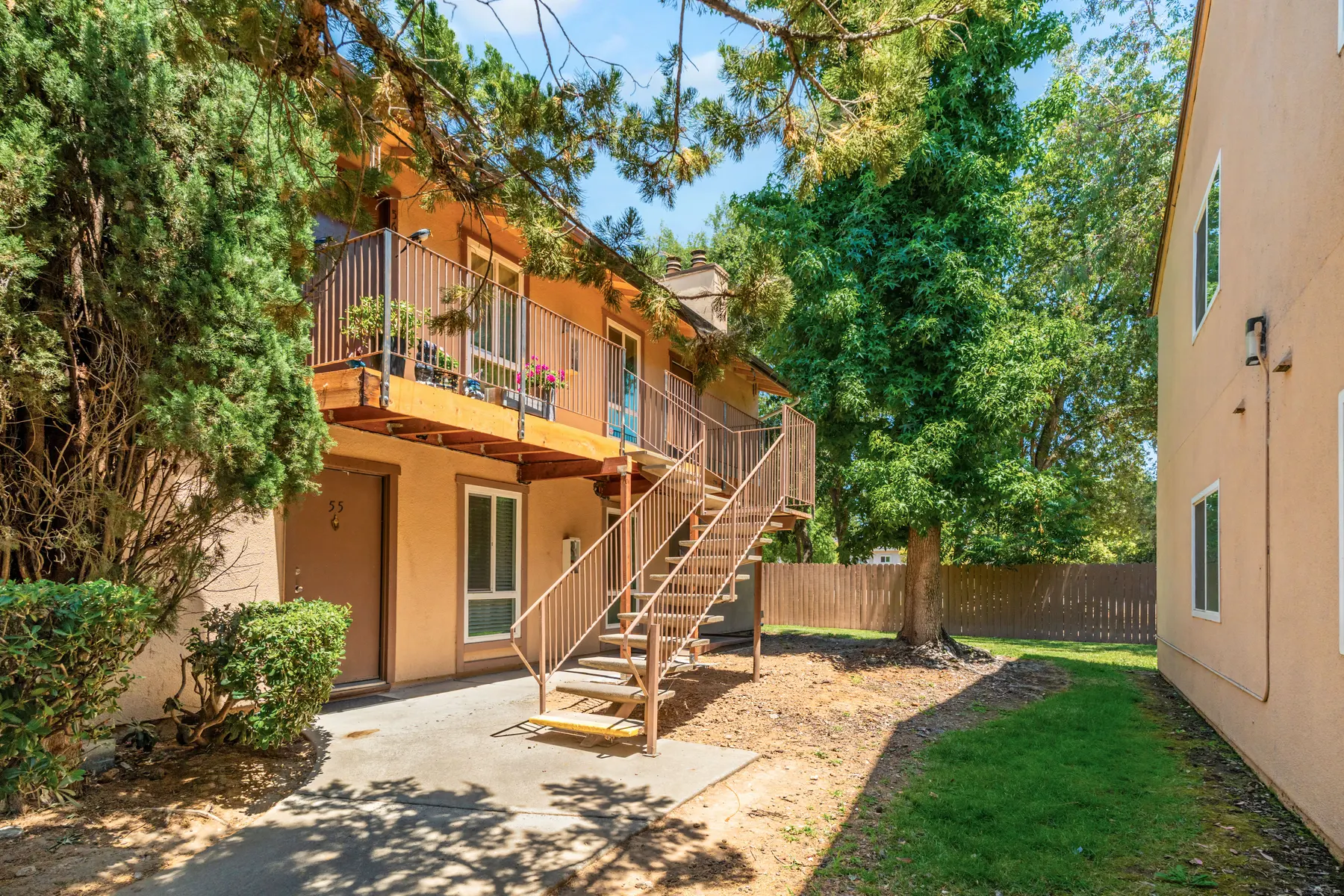 Ground-level view of an apartment building with a staircase, surrounded by trees and a grassy area.