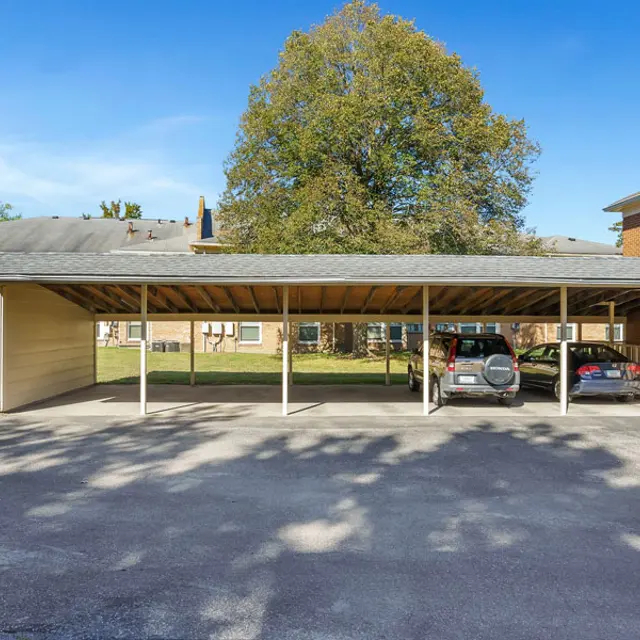 A carport with two parked cars underneath it and green grass in the surrounding area.