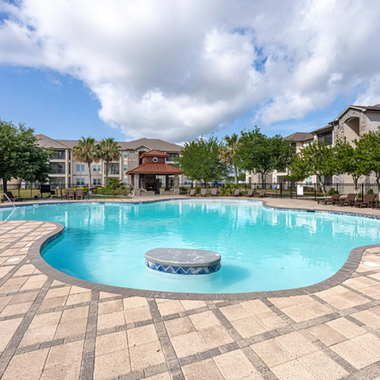A spacious outdoor swimming pool surrounded by tiled patio and lush greenery.
