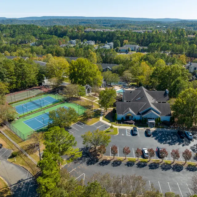 Aerial view of a tennis center with two courts, surrounded by greenery and residential buildings in the background.