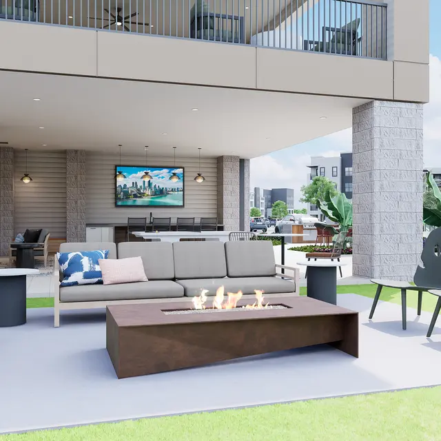 A modern outdoor living space featuring a seating area with a sofa and fire pit, under a covered patio with plants and an outdoor television.