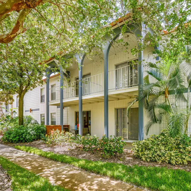 A landscaped view of an apartment complex featuring a two-story building with balconies, surrounded by greenery and pathways.