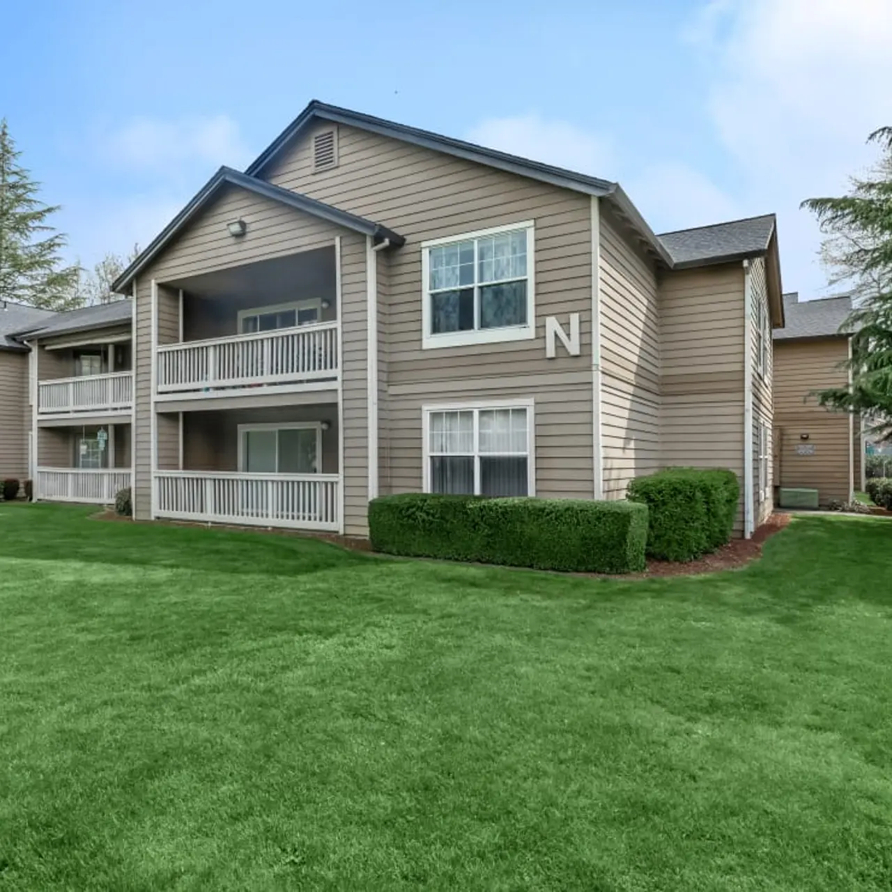 Exterior view of a beige apartment complex with multiple buildings and lush green grass.