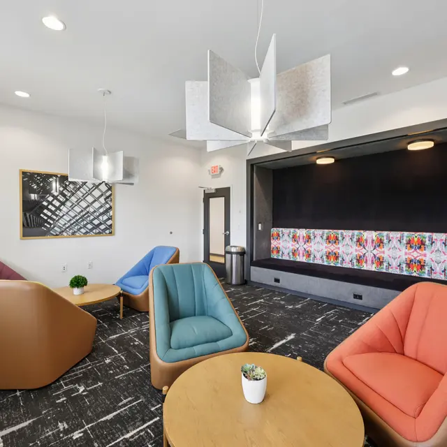 Contemporary Lounge Space A contemporary lounge area featuring colorful triangular chairs and a wooden table. A decorative light fixture hangs above, and a vibrant wall art displays colorful patterns.
