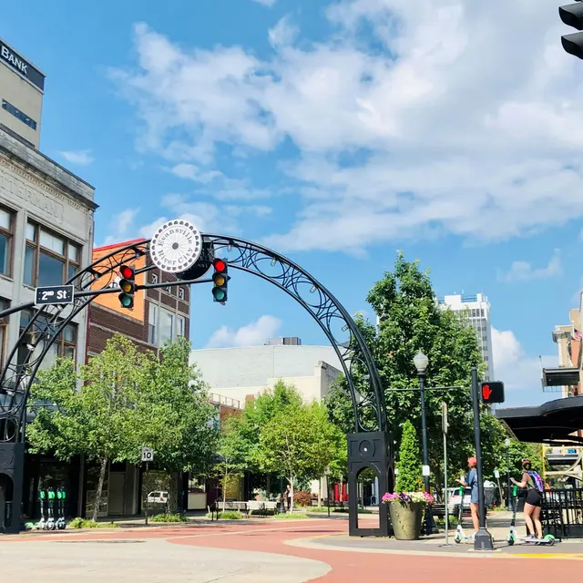 A street view featuring an archway with traffic lights and greenery in a busy downtown area.