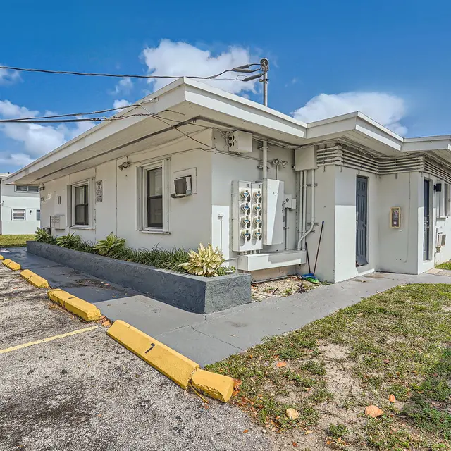 Exterior view of a modern apartment complex with a red car parked in front and landscaping surrounding the entrance.