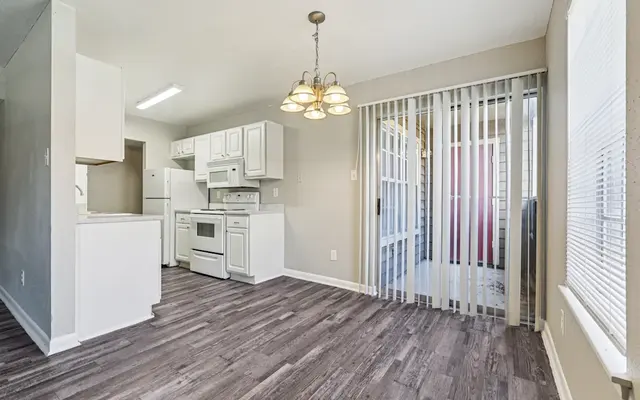 Modern Kitchen and Dining Area A modern kitchen and dining area featuring white cabinetry and appliances, a wooden floor, and a sliding door.