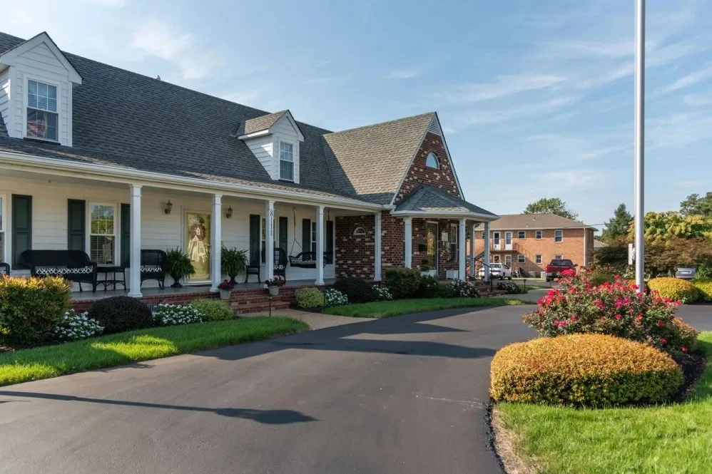 A charming house with a porch and landscaped front yard, featuring green grass and blooming flowers.