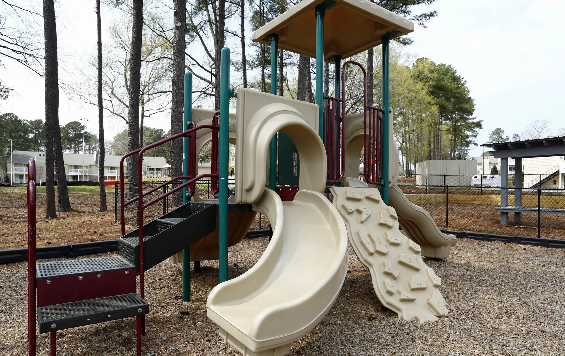 Playground structure with two slides and a climbing area surrounded by trees.