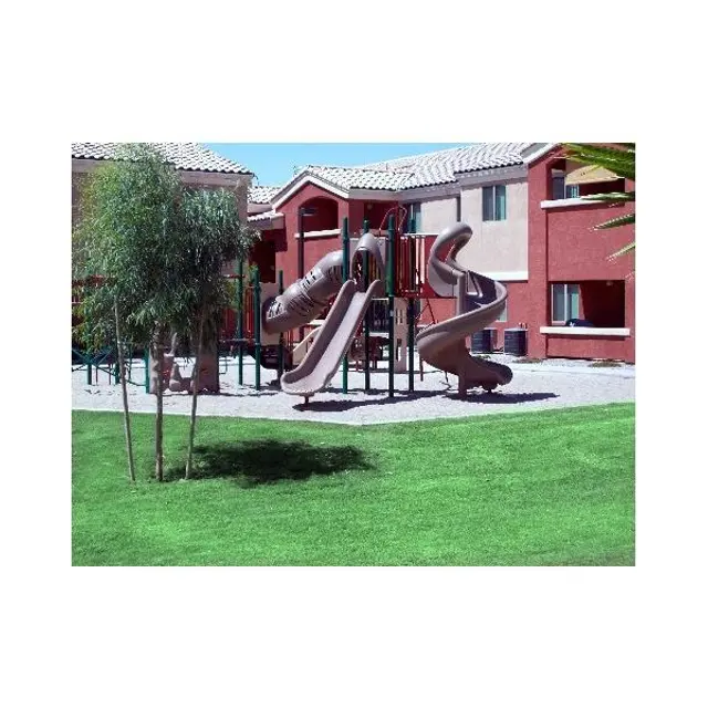 A playground featuring multiple spiral slides surrounded by green grass and buildings in the background.