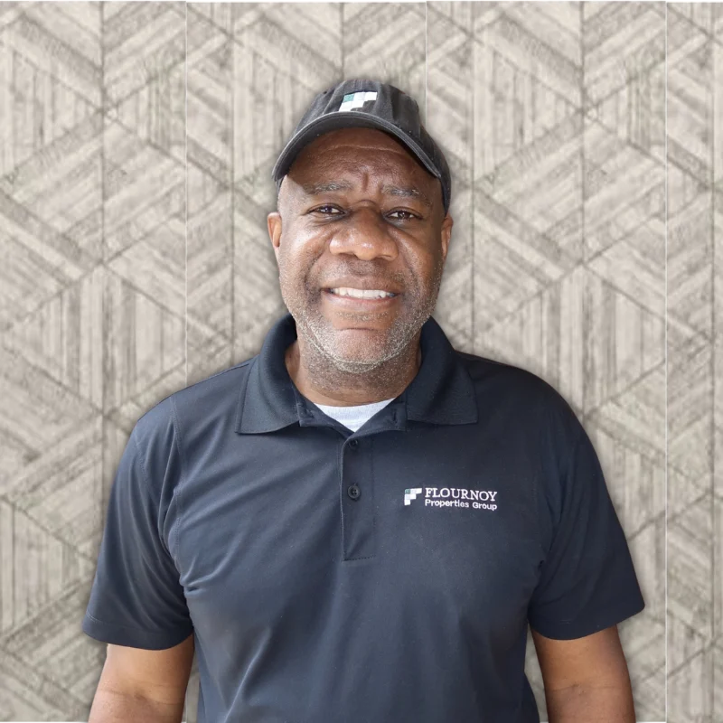 Professional Individual in Branded Attire A man wearing a black polo shirt and cap with the logo of a property group stands in front of a patterned background.