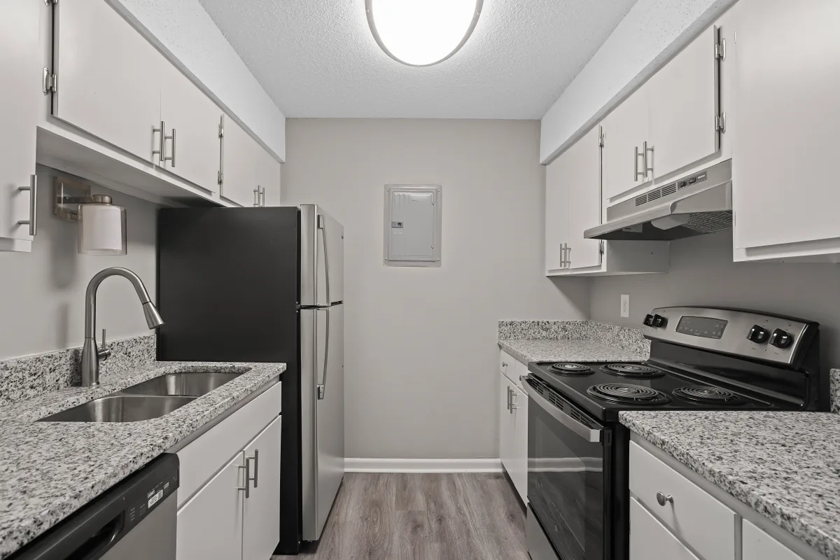 A modern kitchen featuring granite countertops, white cabinets, stainless steel appliances, and laminate flooring.