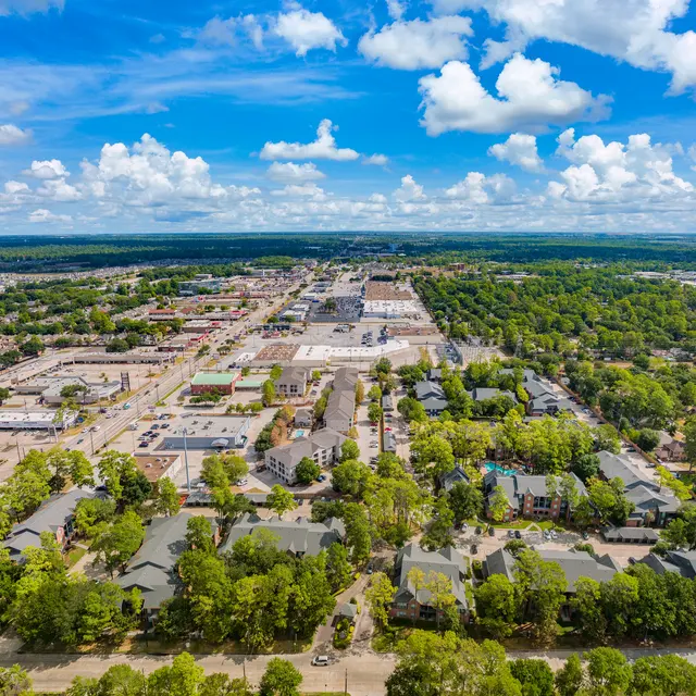 Aerial view of a city featuring numerous buildings, roads, and green trees under a partly cloudy sky.
