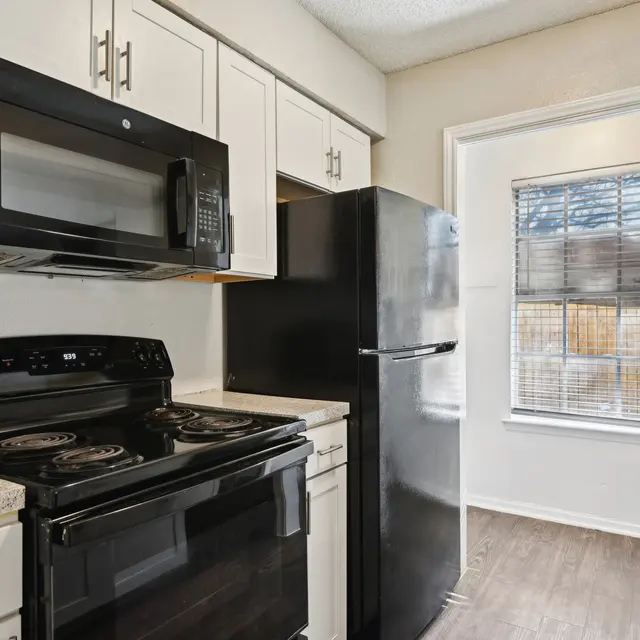 A modern kitchen featuring black appliances including a microwave, oven, and refrigerator, with white cabinets and a window allowing natural light.