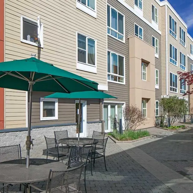 A view of an outdoor seating area with tables and umbrellas next to a modern apartment building.