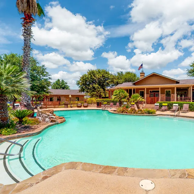 Resort Pool Area A clear swimming pool surrounded by palm trees and lounge chairs under a bright blue sky with fluffy white clouds.