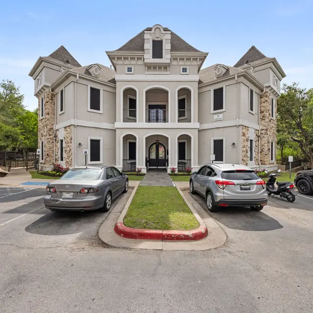 A historic building with a multi-story structure featuring a decorative facade, surrounded by parked cars including a motorcycle and a green lawn.