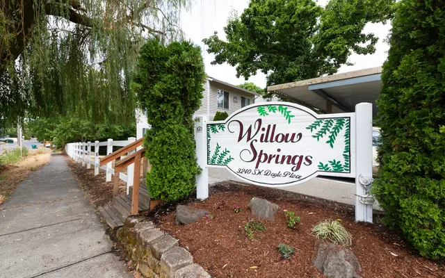 Sign for Willow Springs with decorative green elements, surrounded by greenery and landscaping.
