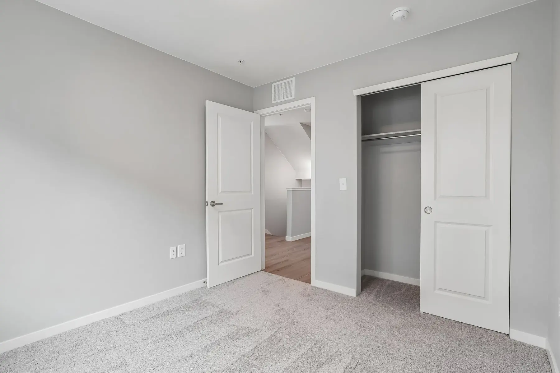 Modern Bedroom Interior A minimalistic bedroom interior with gray walls and carpeted flooring. The room features an open door leading to a closet and another doorway in the background.