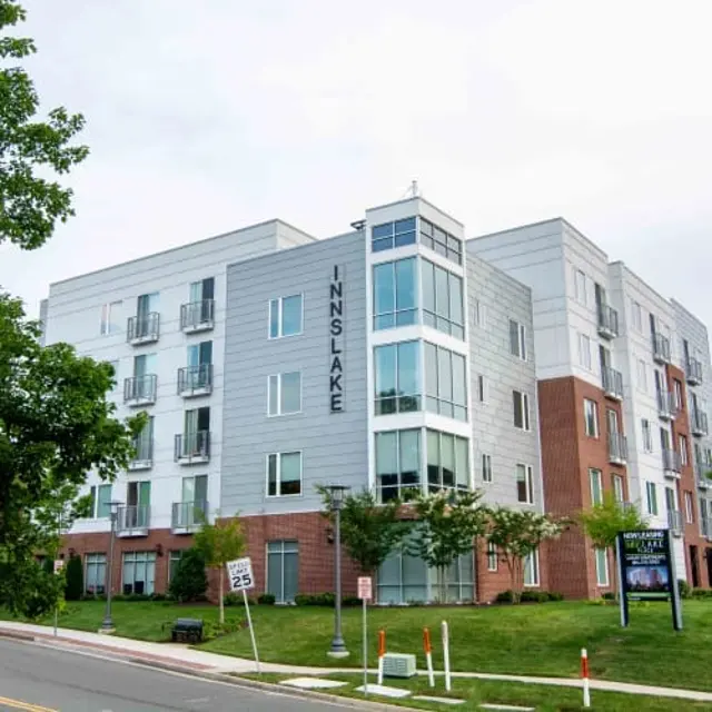 Modern apartment building with a mix of brick and siding, featuring balconies and green landscaping.