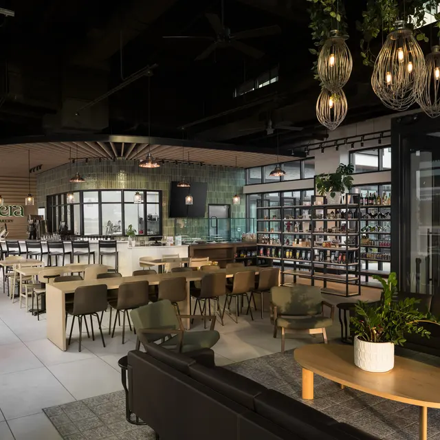 Casera Cafe & Bakery A stylish restaurant interior featuring wooden tables, modern furniture, and a bar area with shelves of drinks.